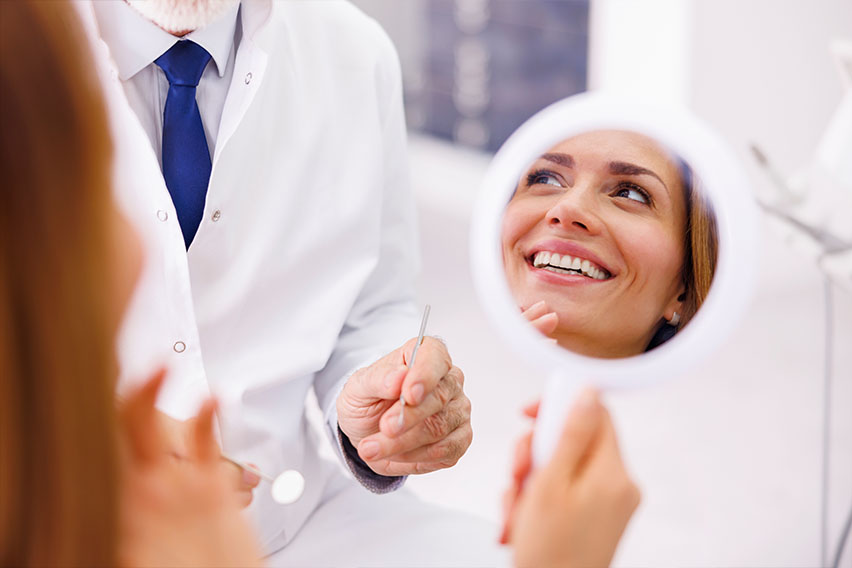 The image shows a dental office interior with a dental chair, overhead lighting, and a monitor displaying what appears to be an X-ray.