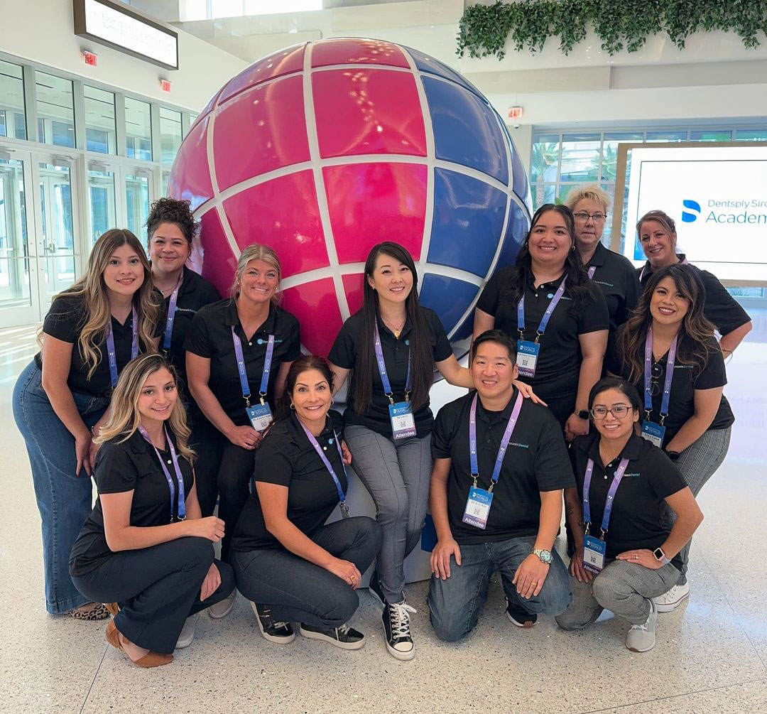 The image shows a group of people posing for a photo with a large, colorful globe in the background. They are standing in front of a sign that reads SAP and appear to be at an event or conference.