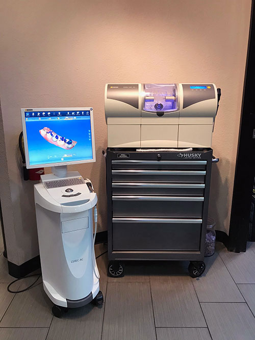 The image shows a dental office setting with a computerized chair for dental work, a counter with a digital display and a printer, and a machine that appears to be used for dental procedures.
