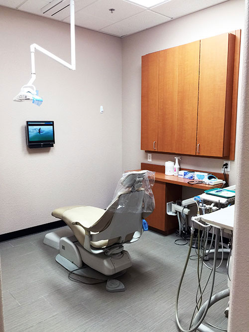 A dental office interior with a modern chair, dental equipment, and a computer screen displaying an image of a mouth.