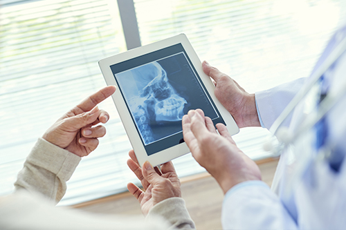 The image shows a medical professional holding a tablet with an X-ray displayed, while another person looks at the screen.